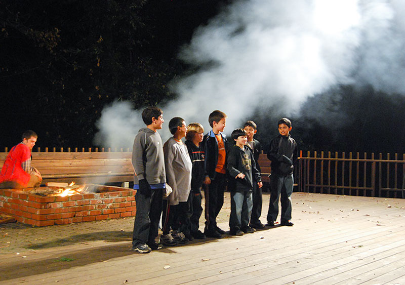 group of boys standing by an outdoor fire